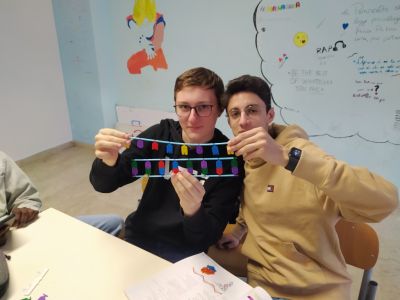 Two boys holding DNA and RNA models between them while sitting at a classroom table